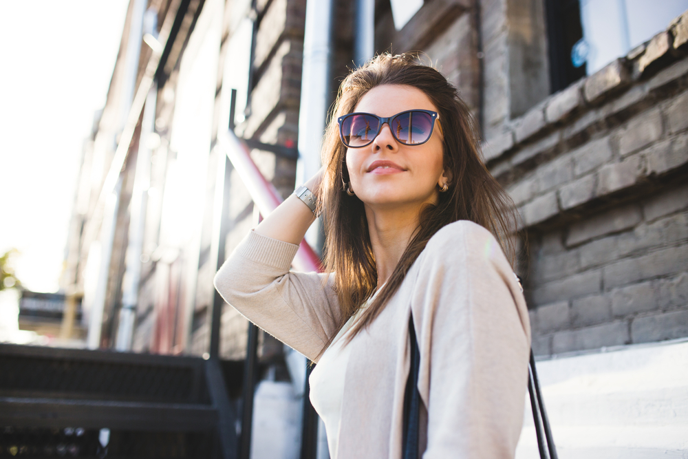 Confident woman wearing stylish sunglasses outdoors near a brick building, representing fashionable eyewear and expert vision care from an optometrist in Palm Desert - Optometrist Palm Desert