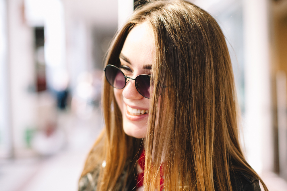 Smiling woman wearing round sunglasses outdoors, showcasing fashionable eyewear and clear vision from Coachella Valley Optometry Indio - Coachella Valley Optometry Indio
